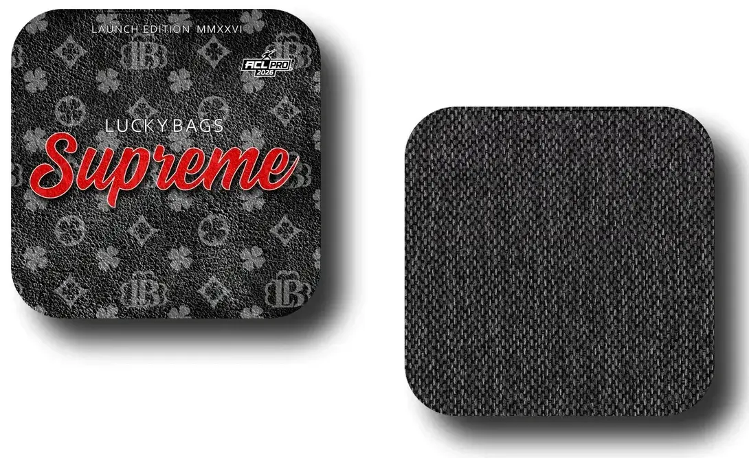Two square cornhole bags displayed side-by-side. The bag on the left shows the graphic side, featuring a black background with a monogram pattern, the text "LUCKY BAGS" in small white letters, and "Supreme" in a large red script font. It also bears an "ACL PRO 2026" stamp. The bag on the right shows the reverse side, consisting of a plain, dark grey woven fabric texture.