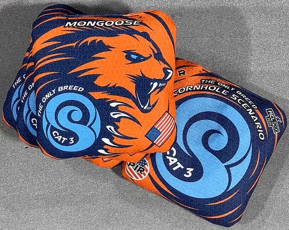 Two orange and blue cornhole bags are displayed against a dark gray background. The top bag, largely visible, features a fierce mongoose head design in blue on an orange background, with "MONGOOSE" written above it. Below the mongoose head, there's a blue circular logo with an "S" and "CAT 3" in white. A small American flag patch is also visible. Part of another bag is seen beneath, also in orange and blue, with "CORNHOLE SCENARIO" visible along a circular design.