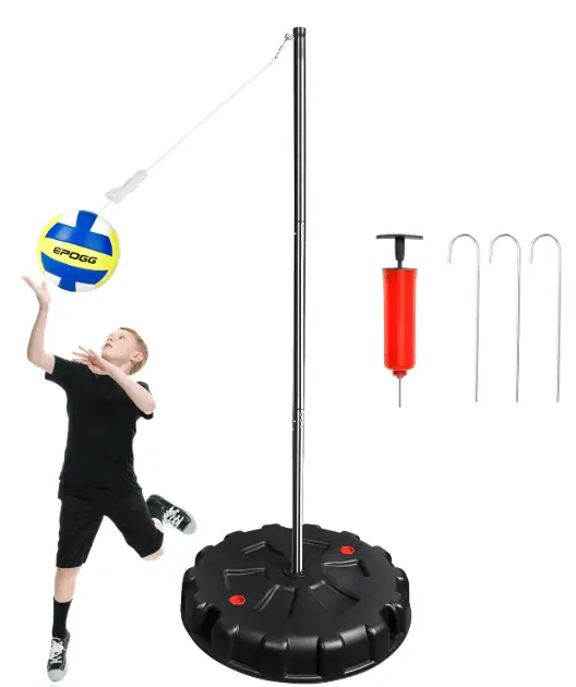 A tetherball set is displayed, including a black base, a tall silver pole, a volleyball suspended by a string, a red hand pump, and three silver ground stakes. A young boy in a black t-shirt and shorts is shown in action, playing tetherball.